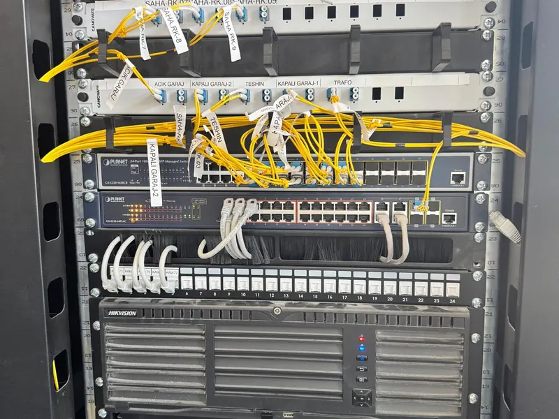 Saha kabineti: etiketli fiber patch panelleri, iki yönetilebilir switch ve Hikvision kayıt cihazları.